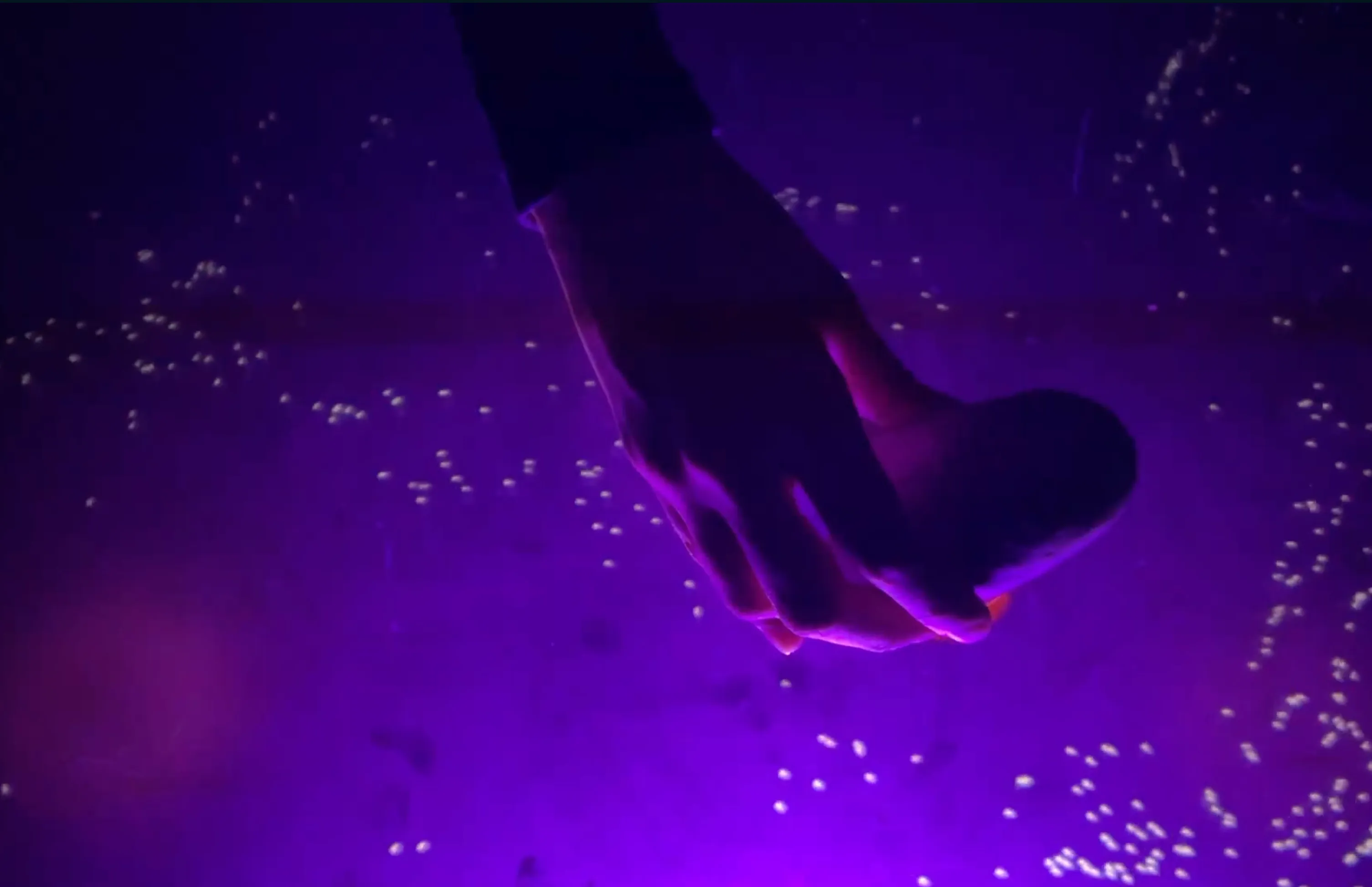 A hand holding an alien-shaped controller on the table, in purple light and particles
