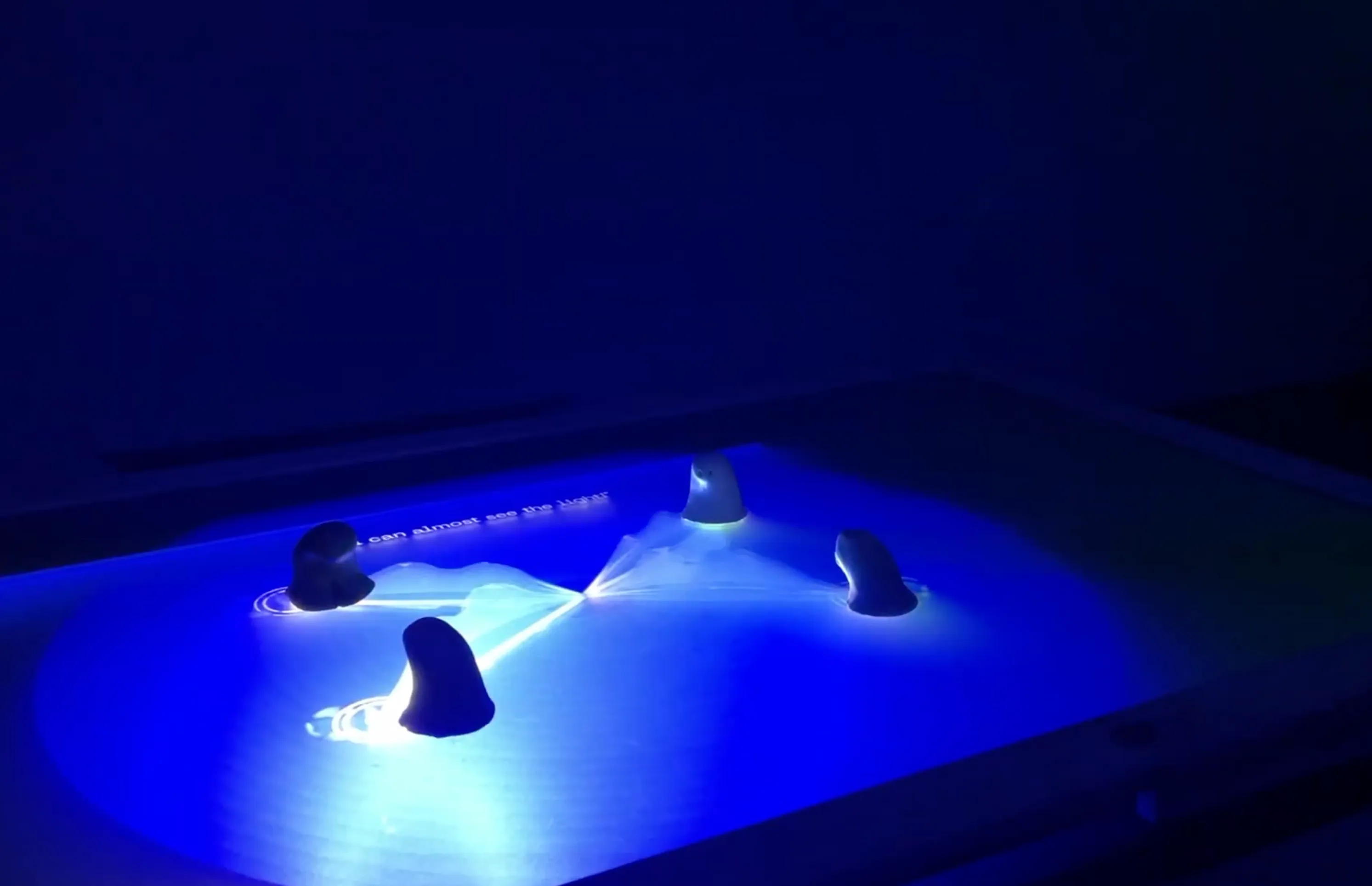 Three alien-shaped controllers on the table, glowing in blue projected light
