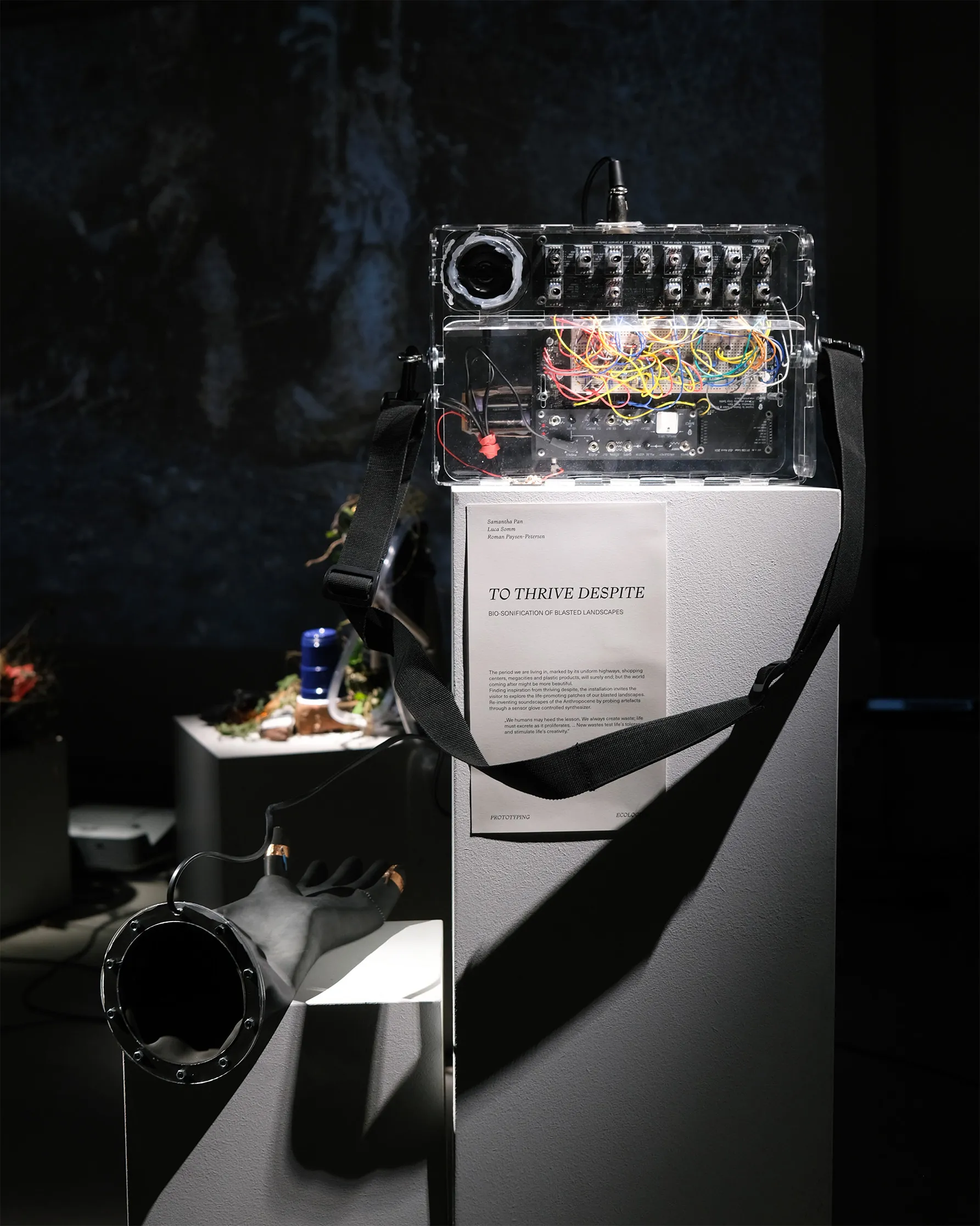 Exhibition space with white pedestal, modular synthesizer on top and a text on the front of the white pedestal
