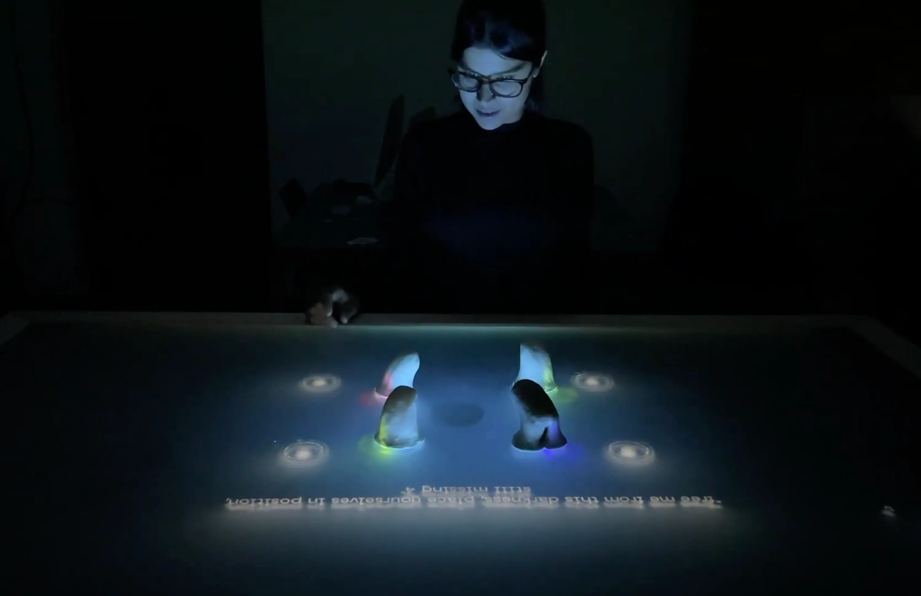A player leaning over the dark interactive table, where glowing alien-shaped controllers stand among projected lights and lyrics